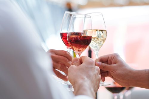 Human hands holding wineglasses with champagne, cabernet and brandy